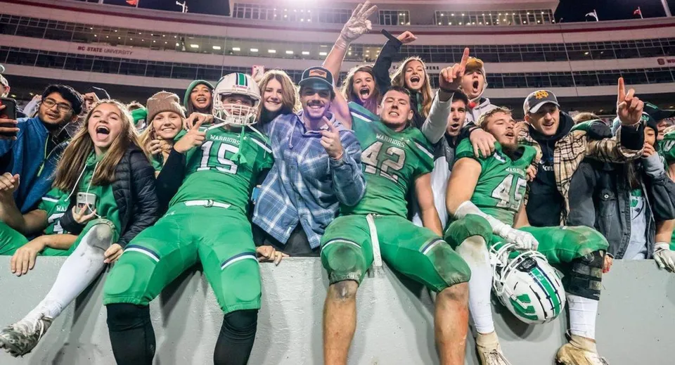 Un gruppo di studenti della St. Mother Teresa High School tifa allo stadio indossando maglie e giacche verdi.