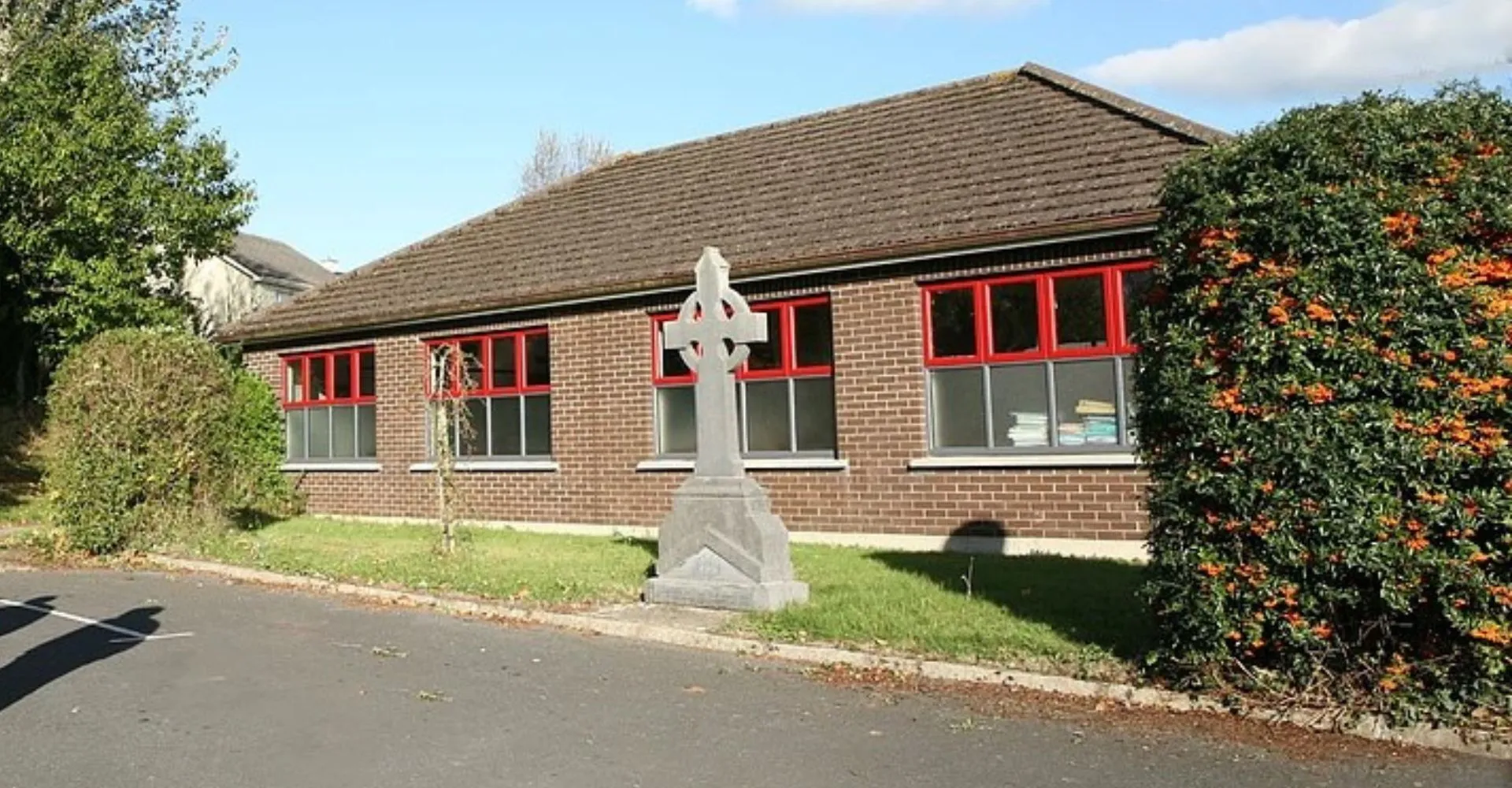 L'edificio in mattoni della Edmund Rice Secondary School è circondato da alberi con una statua in primo piano.