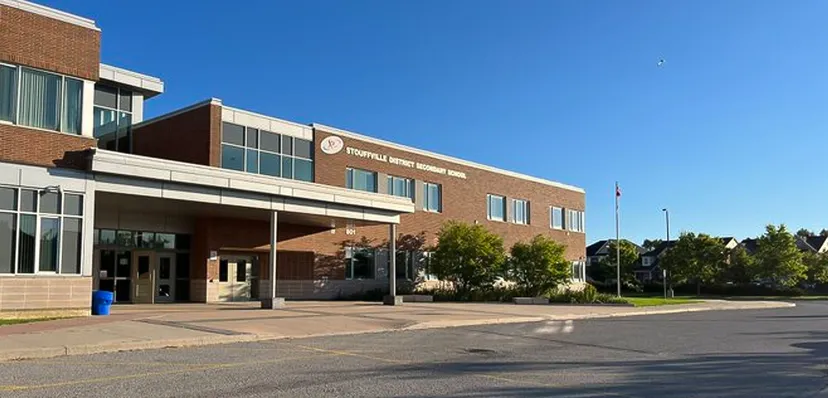 Il grande edificio in mattoni con l'ingresso principale della Stouffville District Secondary School è circondato da alberi e da un'area pavimentata.