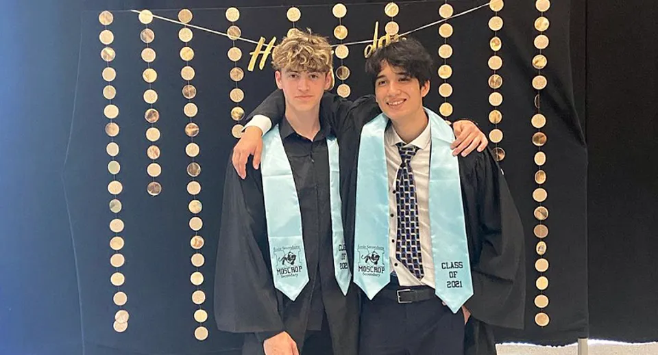 Due giovani uomini in abito elegante si trovano davanti a uno sfondo decorativo durante un evento della Moscrop School.