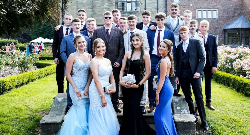 Un grupo de personas vestidas formalmente en el campus del St. Lawrence College frente a un jardín verde.