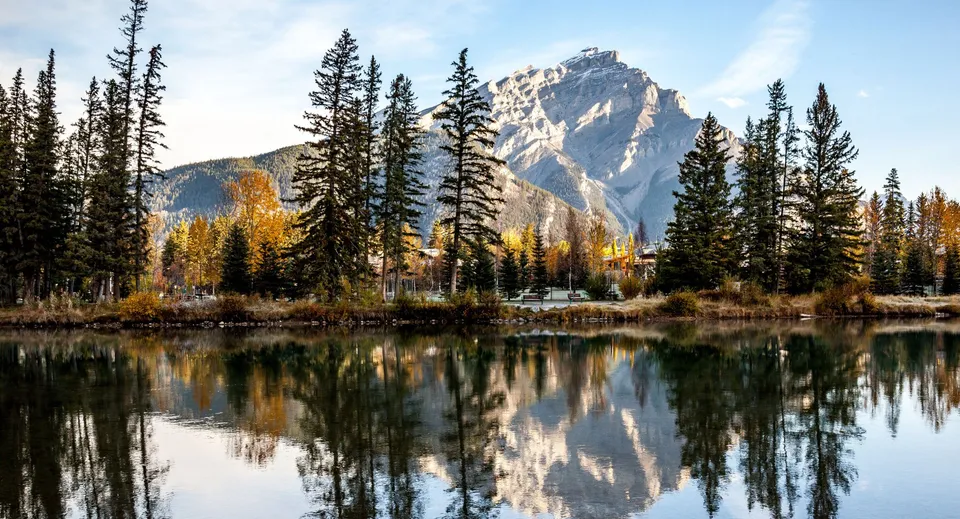Un tranquillo lago di montagna circondato da pini con una cima innevata che si riflette nell'acqua.