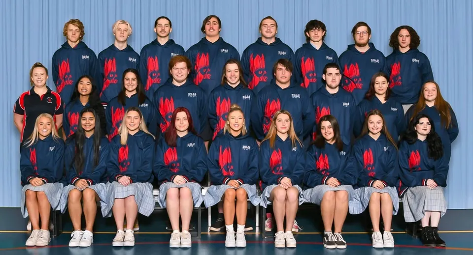 Un gruppo di studentesse in divise uniformi posa davanti a una parete blu nel campus della Roxby Downs Area School.