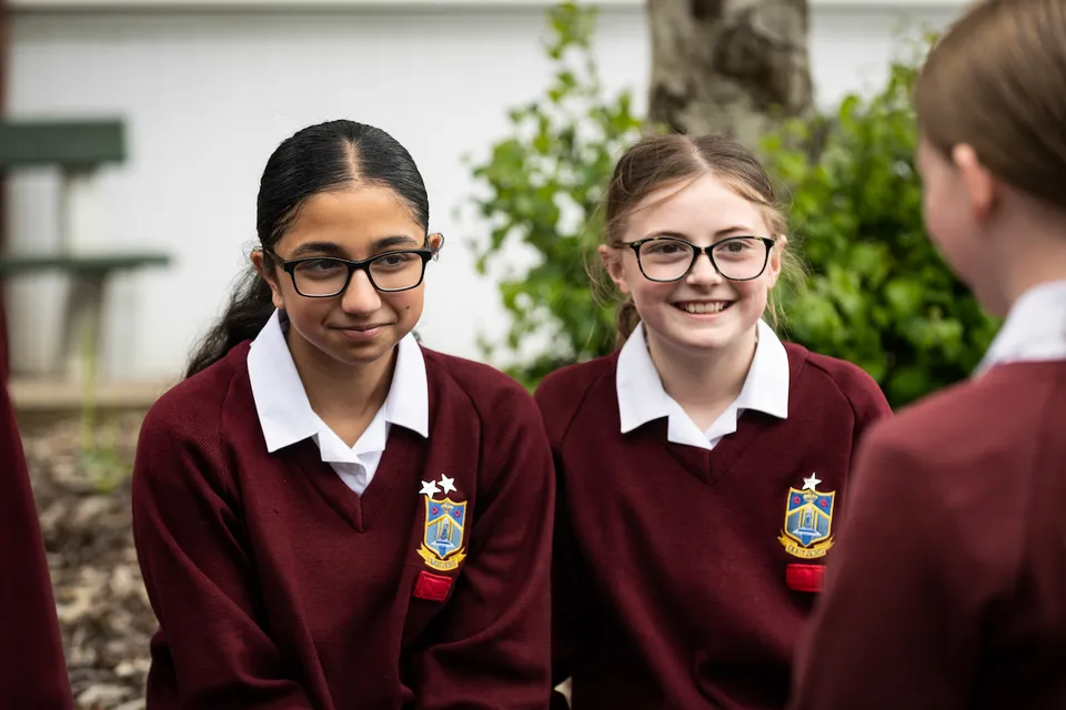 Due studentesse in divisa scolastica sono in piedi su un prato nel campus dell'Our Lady Catholic College.