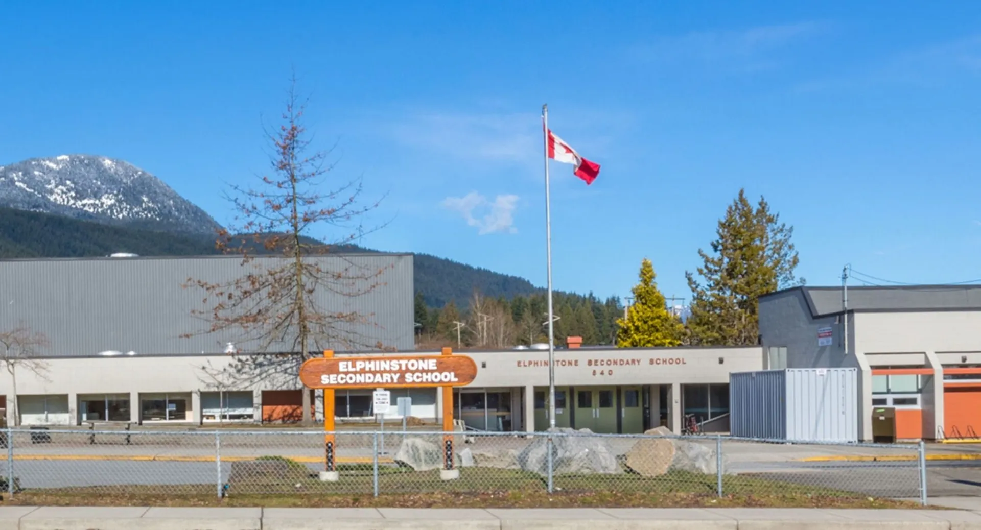 L'edificio moderno della Elphinstone Secondary School con una bandiera canadese e le montagne sullo sfondo.
