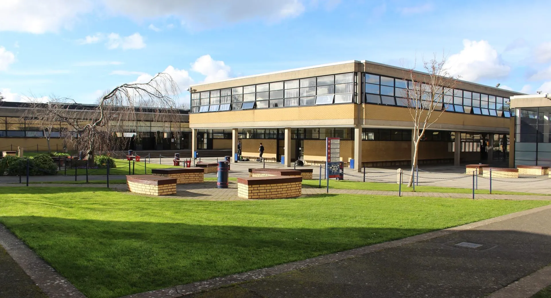 Un moderno edificio a più piani con grandi finestre nel campus del Wesley College è circondato da un prato verde e panchine.