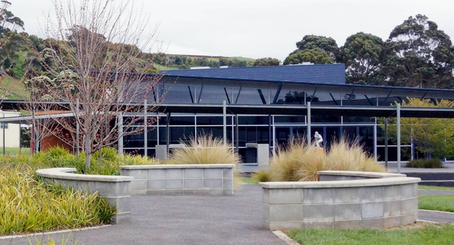 L'edificio moderno in vetro e acciaio con tetto inclinato nel campus della Burnie High School è circondato da giardini ben curati.