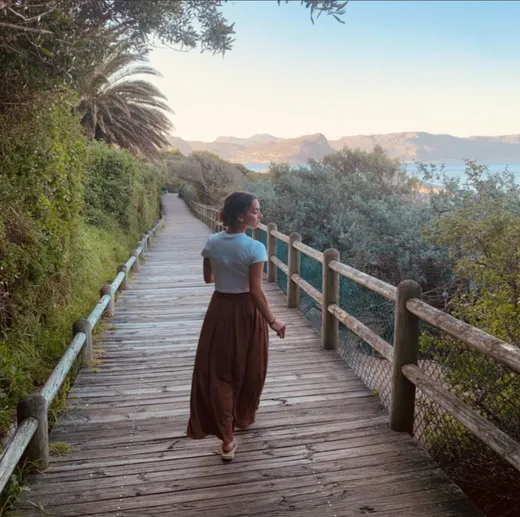 Studentessa cammina su una passerella di legno tra la vegetazione costiera al tramonto in Sudafrica