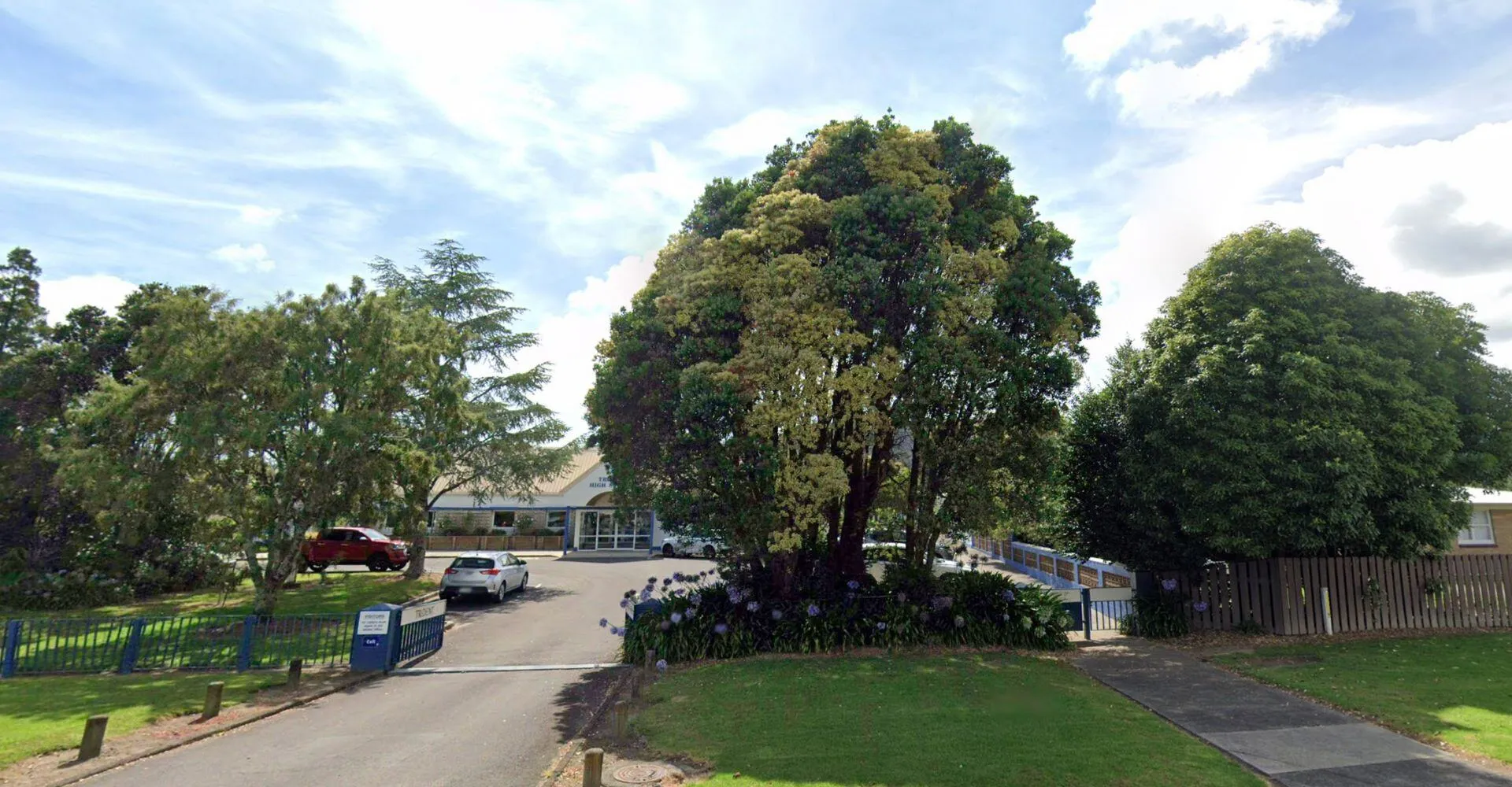 Un sentiero pavimentato conduce attraverso alberi verdi a un edificio nel terreno della Trident High School.