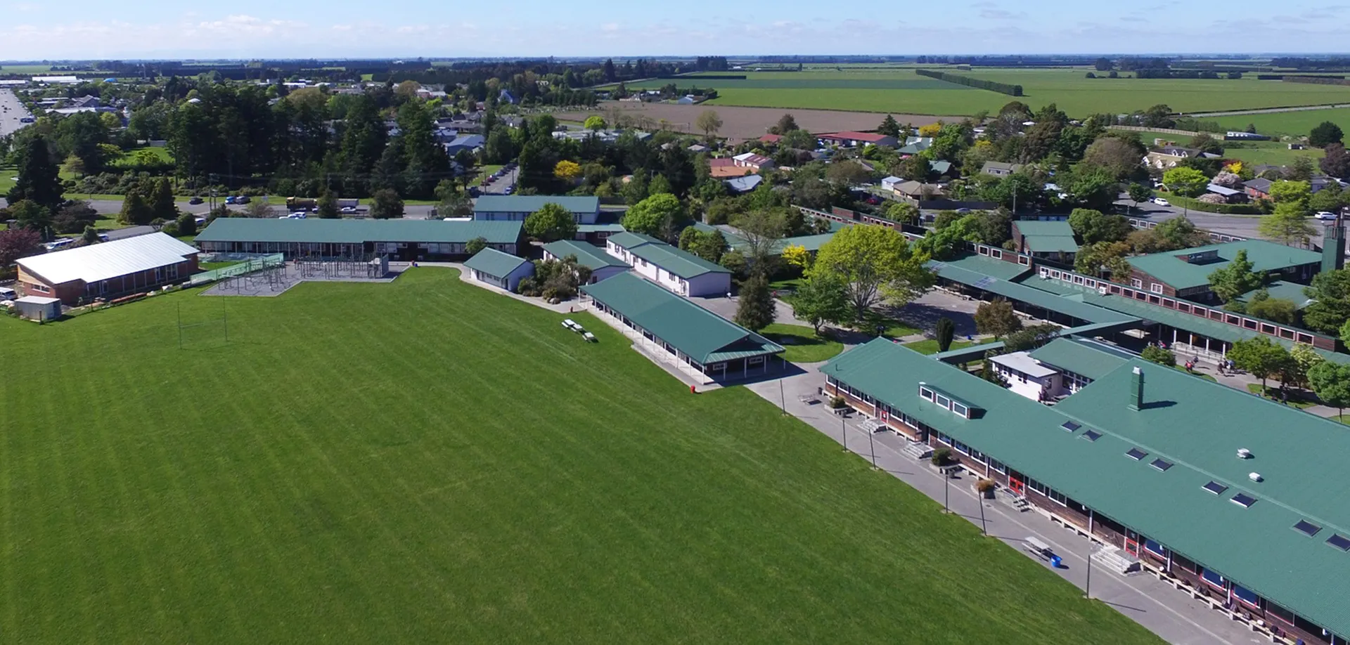 Paesaggio con campi verdi ed edifici davanti a colline alberate all'interno del campus della Darfield High School.