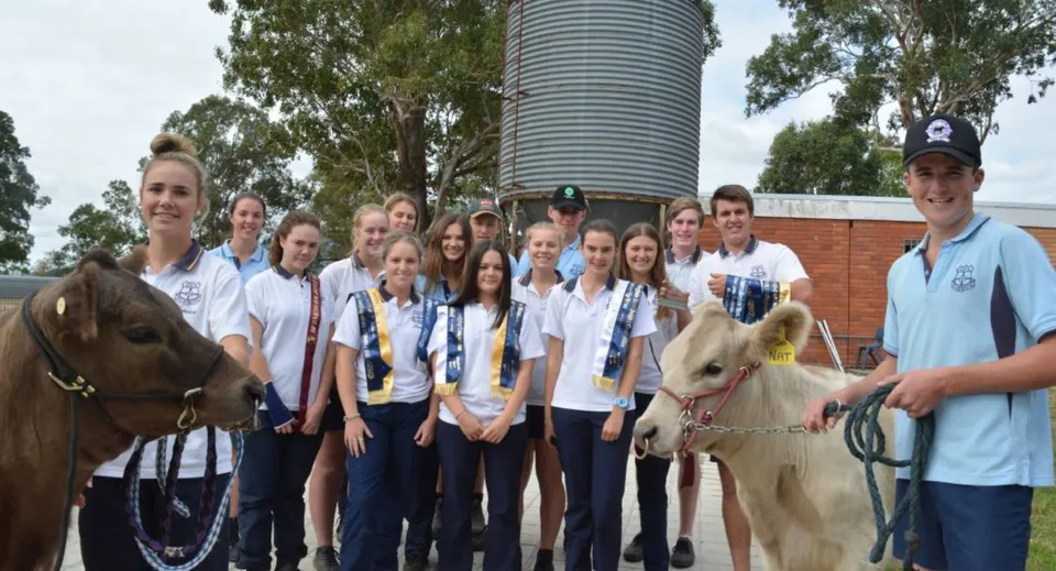 Un gruppo di studenti della Gloucester High School posa con animali davanti a un grande silos di metallo in un ambiente rurale.