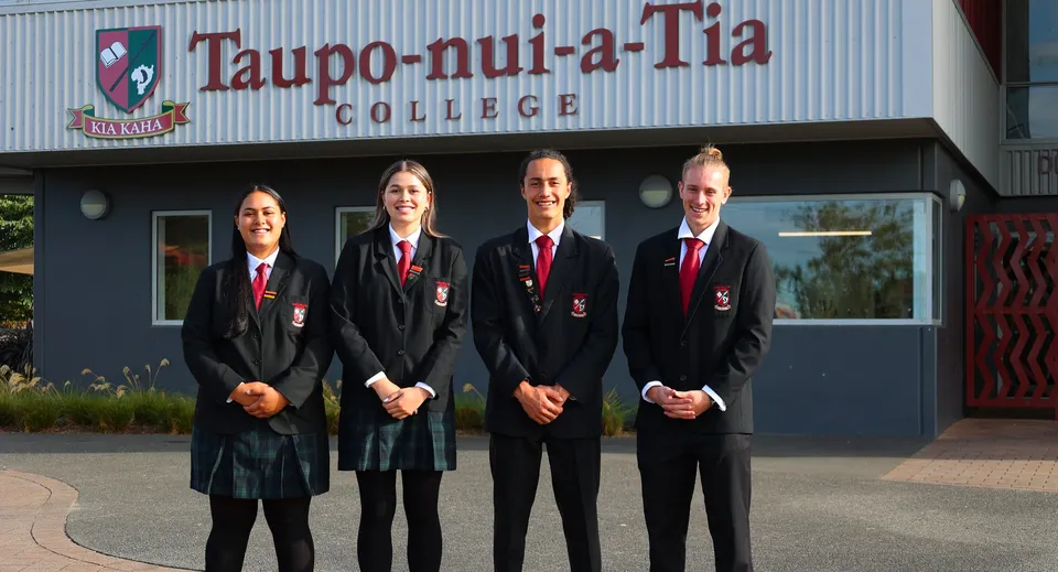 Quattro persone in abiti formali si trovano davanti all'edificio del Taupo-nui-a-Tia College.