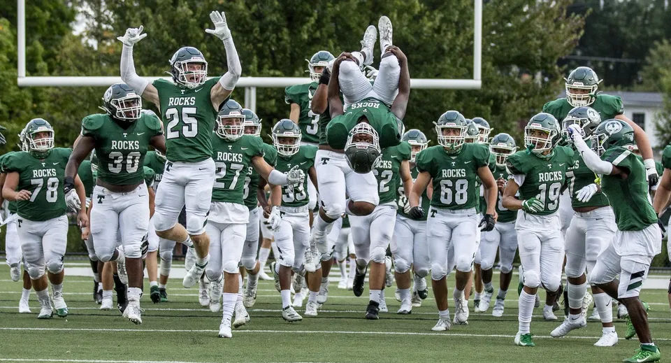 Un gruppo di giocatori di football in uniformi verdi e bianche corre sul campo di gioco del Provo City School District.