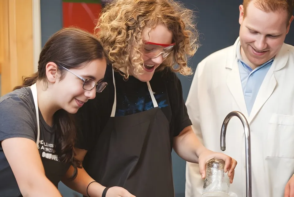 Tre persone lavorano insieme in un laboratorio della St. George's School of Montreal con scaffali e attrezzature sullo sfondo.