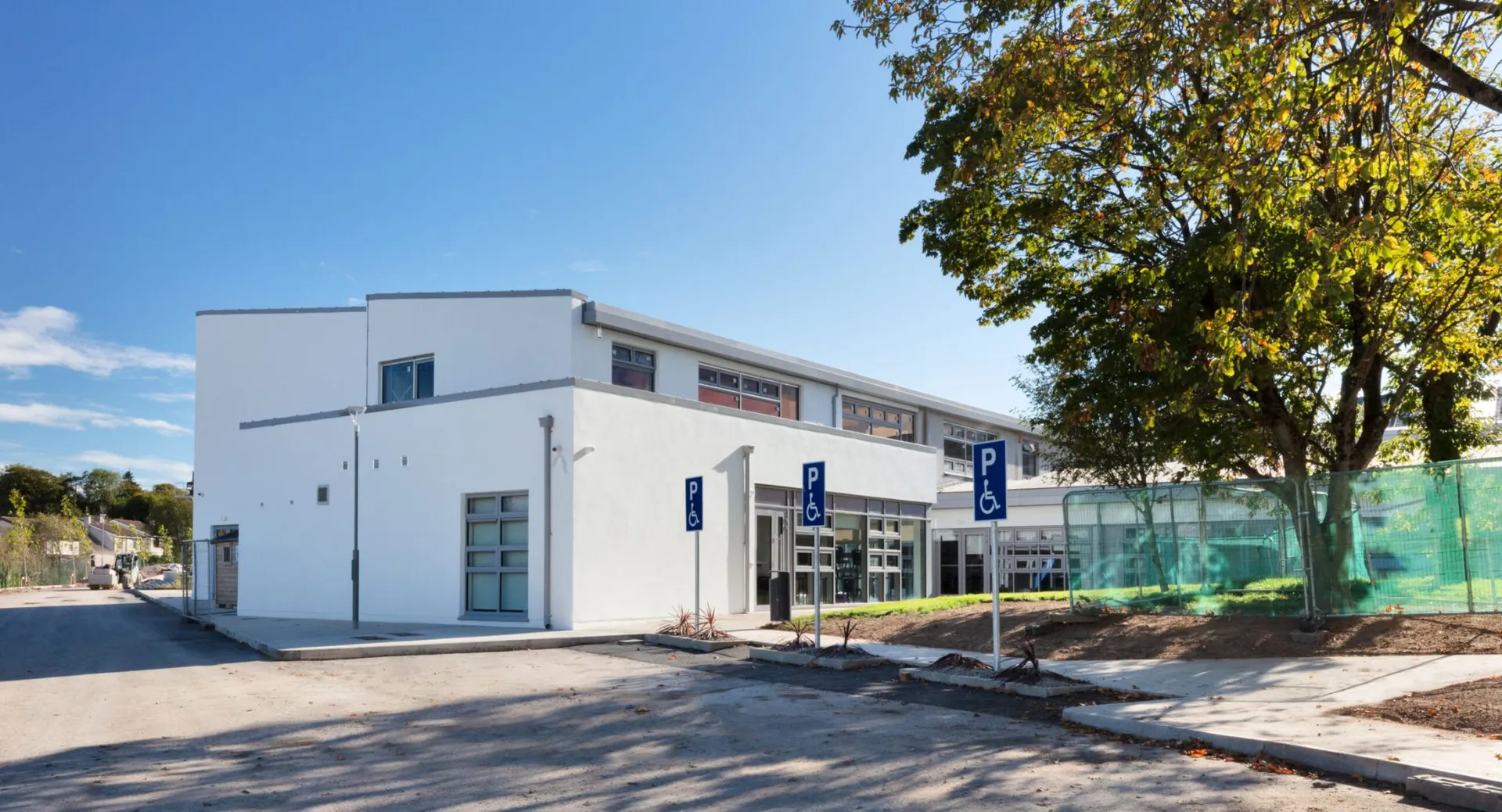 L'edificio moderno e bianco del Midleton College con parcheggi dedicati ai disabili e un grande albero.