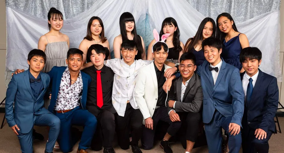 Un gruppo di studenti della Hillmorton High School posa in abito formale davanti a tende bianche.