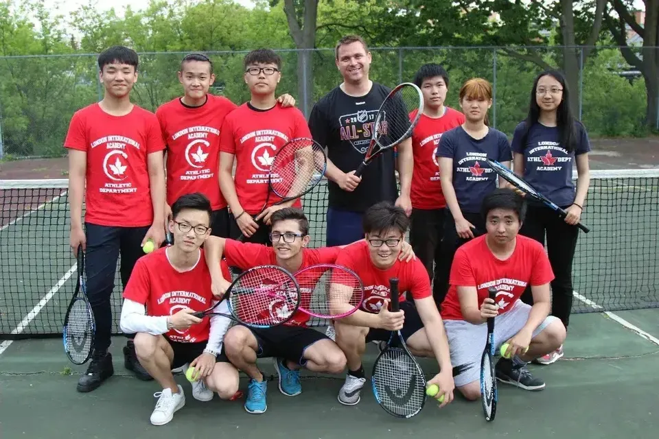 Un gruppo di studenti della London International Academy posa per una foto di gruppo sul campo da tennis indossando magliette rosse.