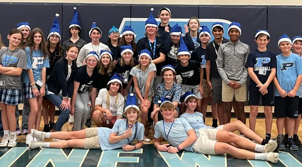 Un gruppo di studenti della Pinewood Preparatory School si trova insieme nella palestra con vari attrezzi sportivi sullo sfondo.