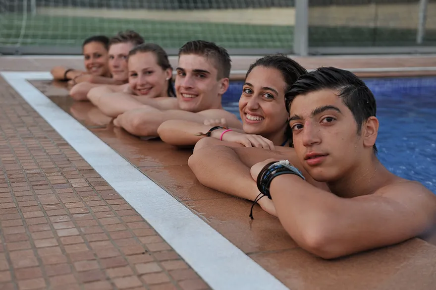 Jugendliche lachen am Beckenrand des Pools der Residencia Teatinos in Málaga