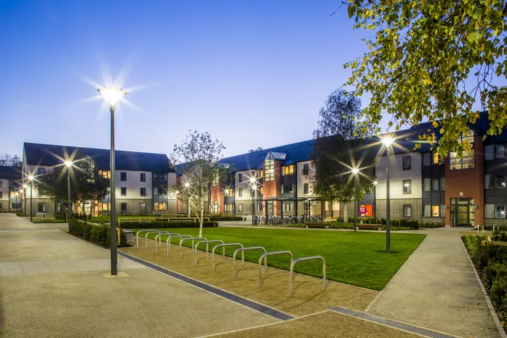 Residenza Belgrove dell'UCD illuminata al crepuscolo con vialetto pedonale e rastrelliere per biciclette