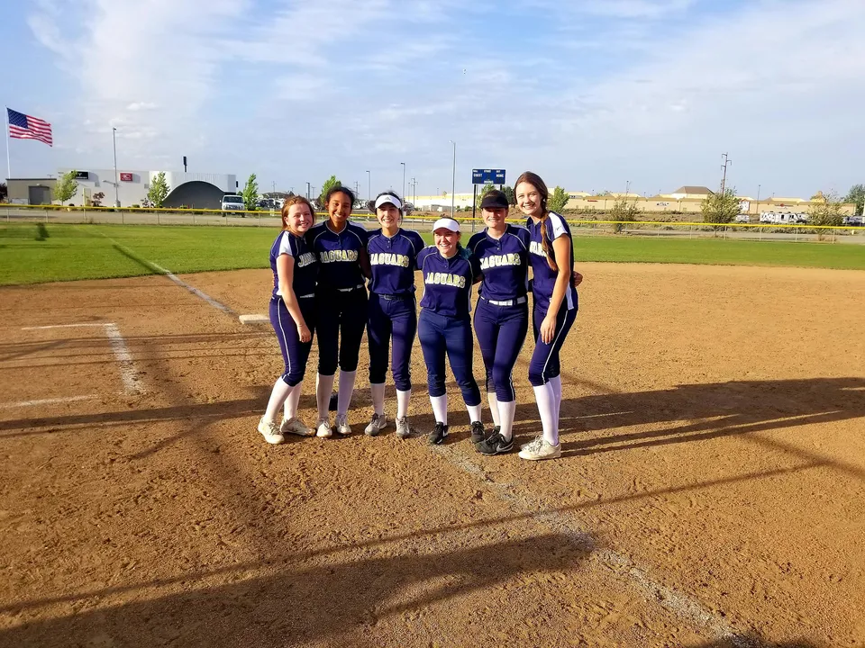 Un gruppo di giocatrici di softball si trova sul campo da gioco della Tri-Cities Prep Catholic High School.