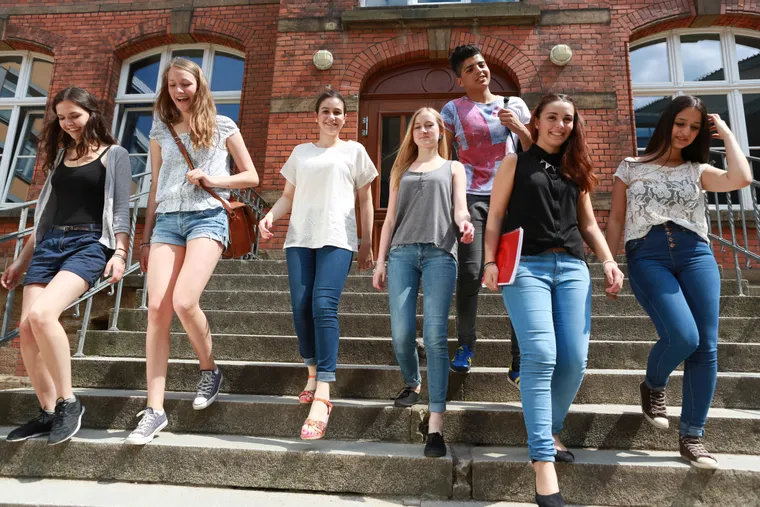 Gruppe lachender Jugendlicher läuft die Steintreppe vor einem Backsteingebäude hinunter