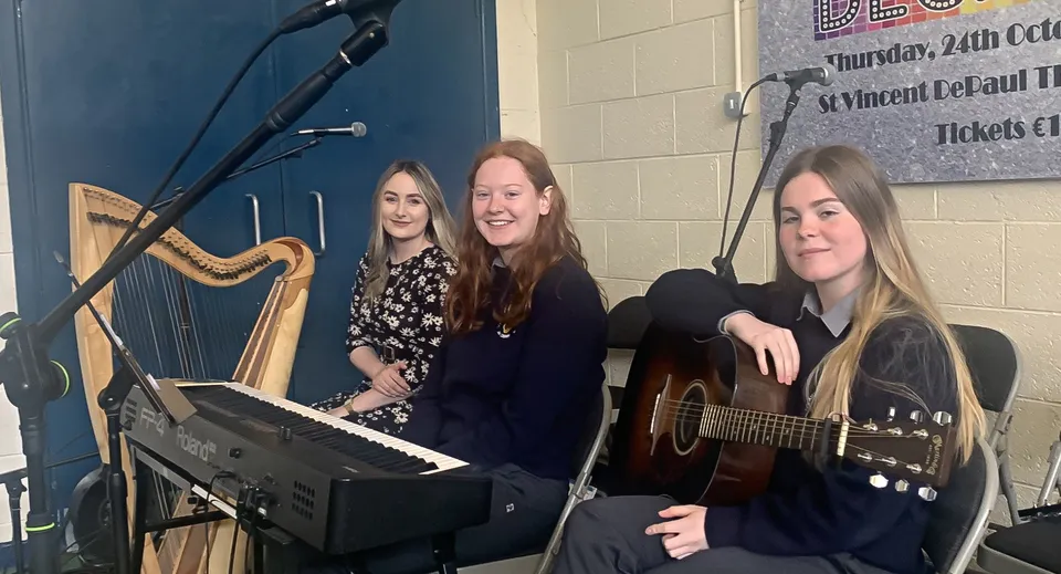 Tre studentesse dell'O’Carolan College si esibiscono insieme sul palco con tastiera e chitarra.