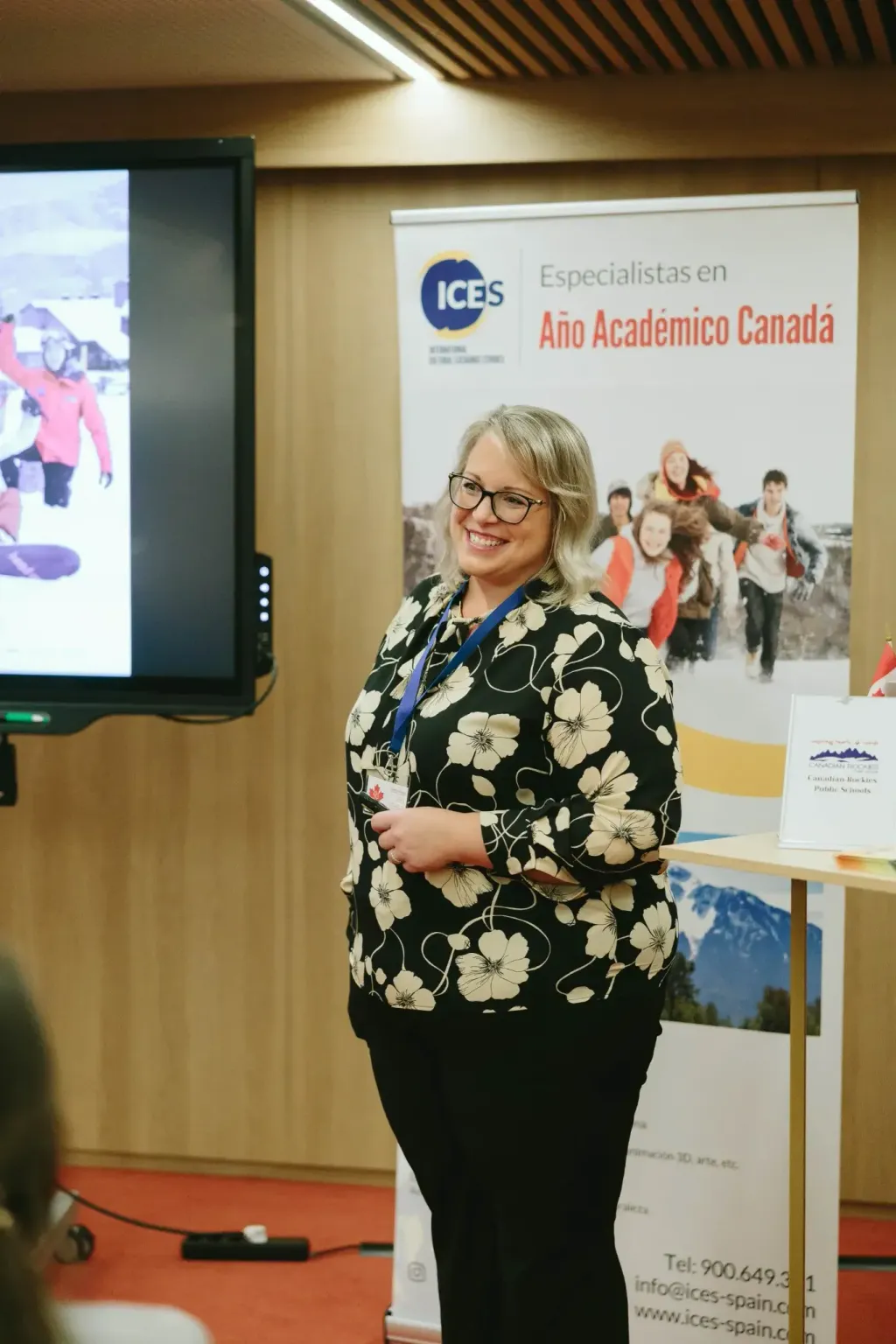 Ponente sonriendo junto a la pantalla y el cartel del año académico en Canadá