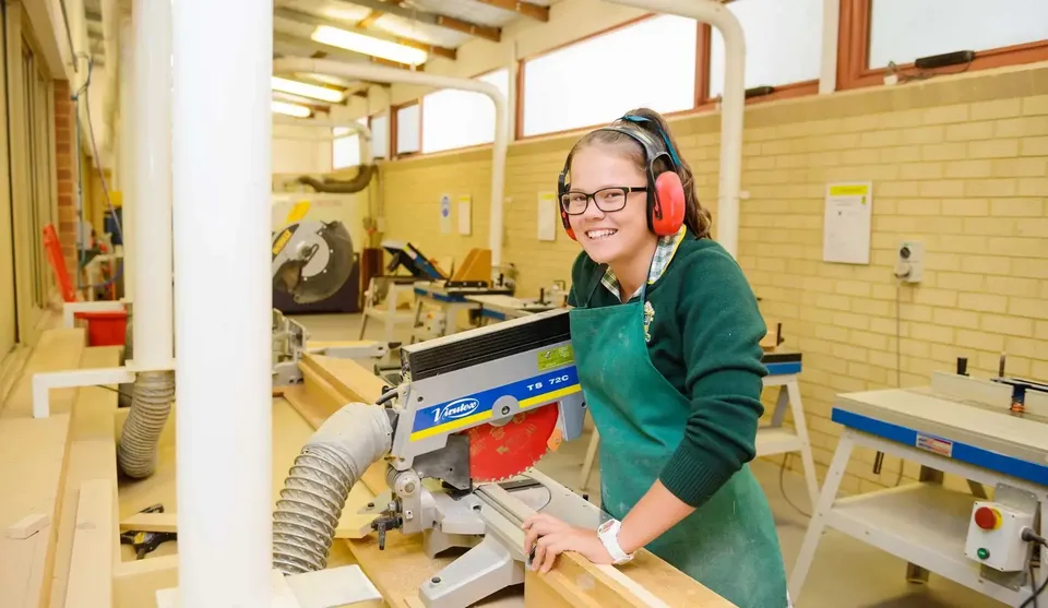 Una studentessa della Frederick Irwin Anglican School lavora con cuffie antirumore a una sega nell'officina.