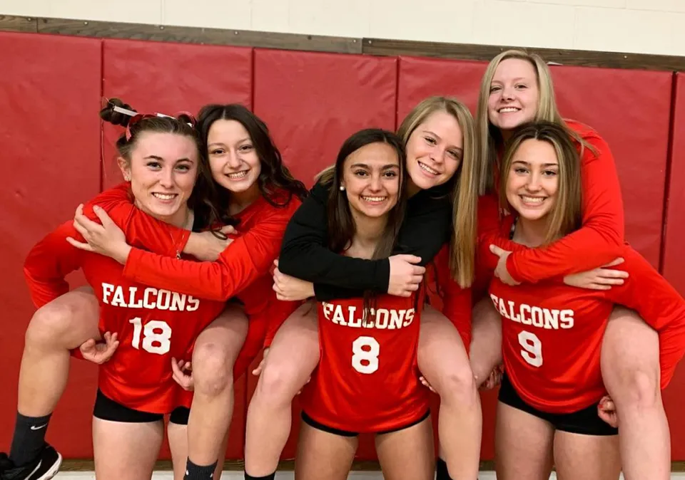 Cinque studentesse della Fabius Pompey High School in maglie sportive rosse dei Falcons posano insieme davanti a uno sfondo rosso.