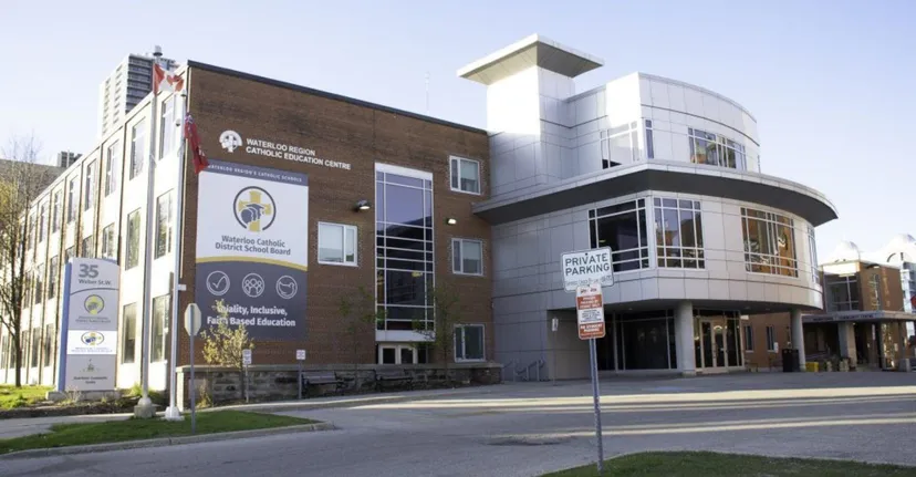 L'edificio moderno a più piani con facciata in mattoni e zona d'ingresso appartiene al Waterloo Catholic District School Board ed è circondato da aree verdi.