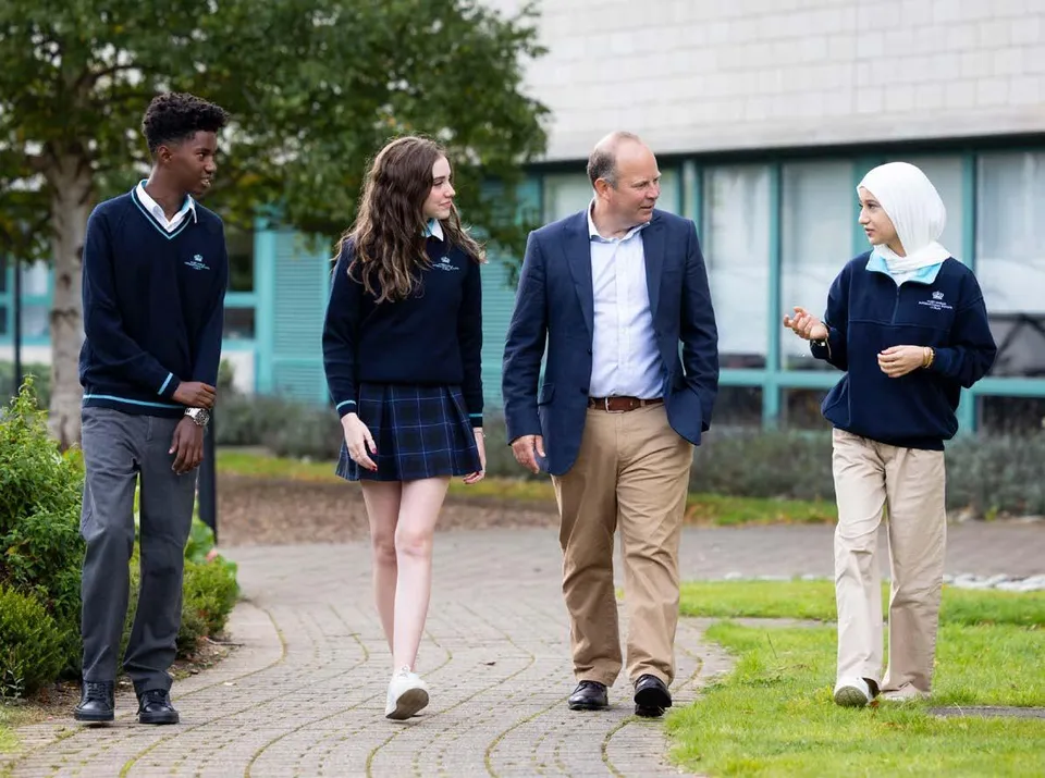 Tre studenti in divisa scolastica e un adulto camminano su un vialetto della Nord Anglia International School Dublin.