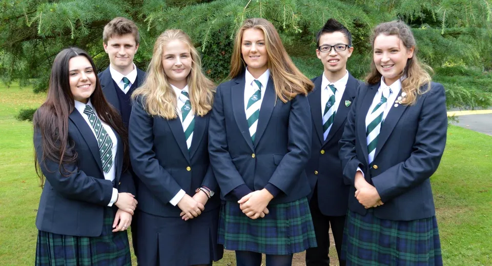 Un gruppo di studenti in divisa scolastica si trova insieme su un prato con alberi sullo sfondo nei terreni della Rockport School.