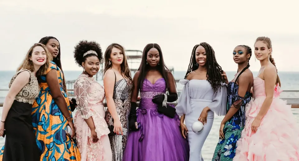 Un gruppo di donne diverse in abiti eleganti posa insieme davanti a uno sfondo bianco alla Roedean School.