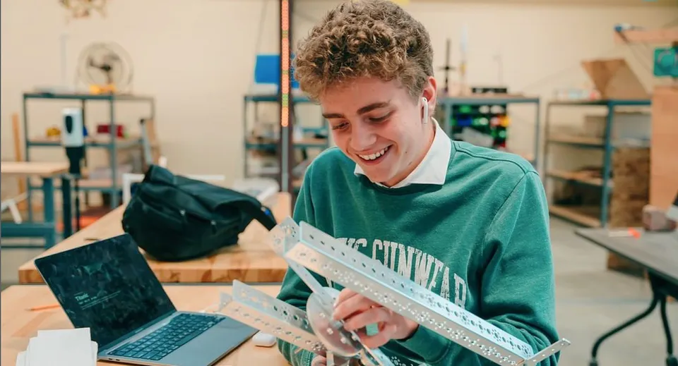 Uno studente della Wasatch Academy lavora sorridendo a un laptop in un'officina.