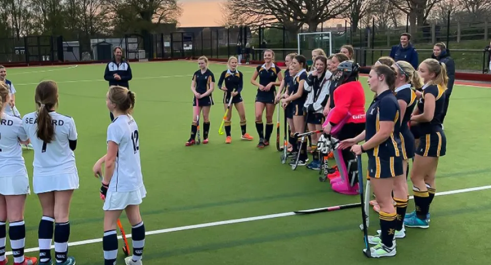 Un gruppo di giovani atlete si trova sul campo sportivo dell'Ardingly College con alberi ed edifici sullo sfondo.