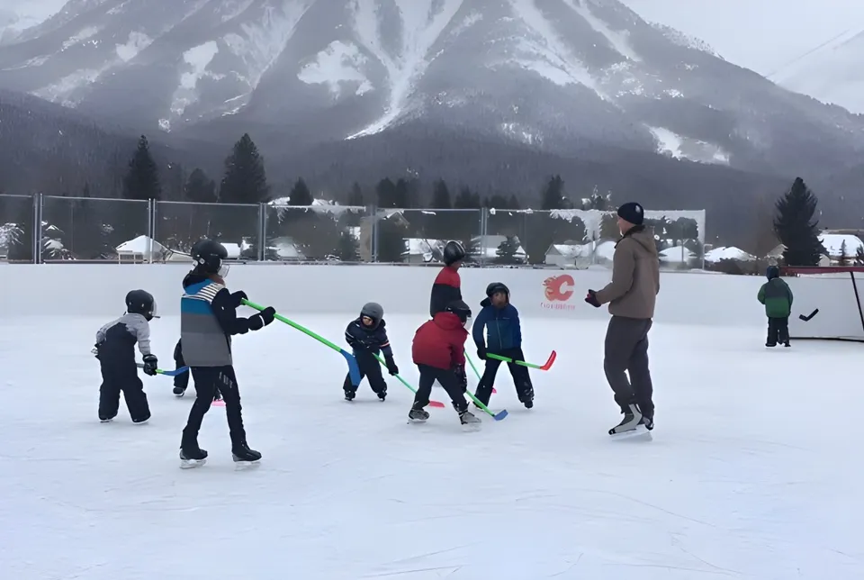 Studenti della École Sophie Morigeau mentre pattinano sul ghiaccio su una pista congelata davanti a un paesaggio montano innevato.