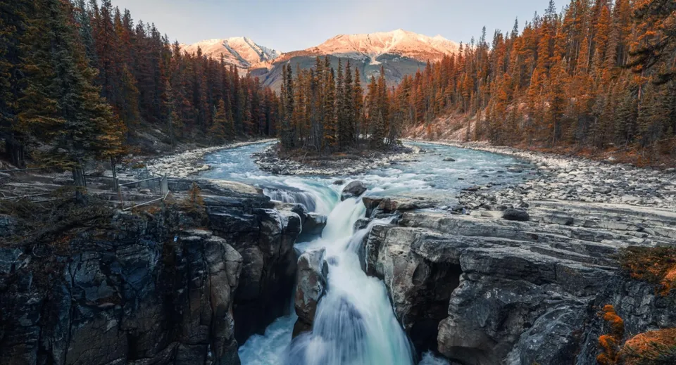 Una maestosa cascata scorre su scogliere rocciose davanti a un paesaggio con alberi sempreverdi e montagne innevate nei pressi della Semiahmoo Secondary School.
