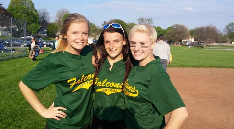 Tre studentesse della The Charles Finney School sono insieme sul campo sportivo con un campo da baseball sullo sfondo.