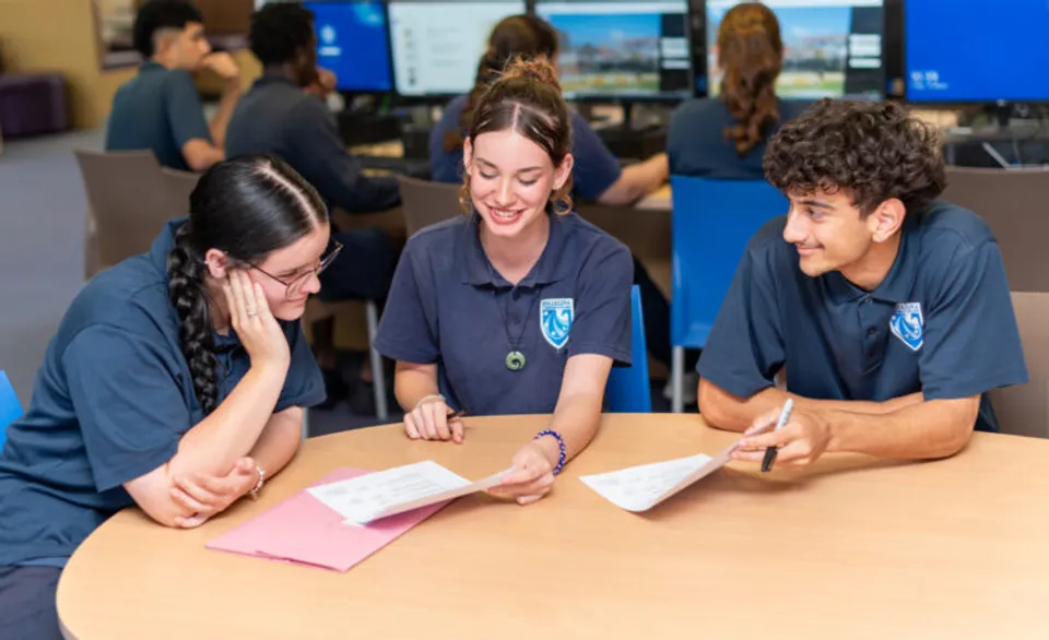 Tre studenti del Ballajura Community College sono seduti a un tavolo e lavorano insieme a un compito in classe.