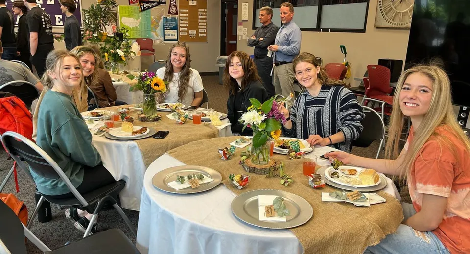 Studenti della Cascade Christian High School sono seduti insieme a un tavolo e mangiano in un ambiente festoso.