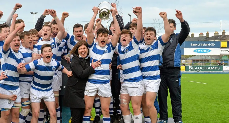 Un gruppo di giovani giocatori di rugby festeggia la vittoria con una coppa sul campo sportivo del Blackrock College.