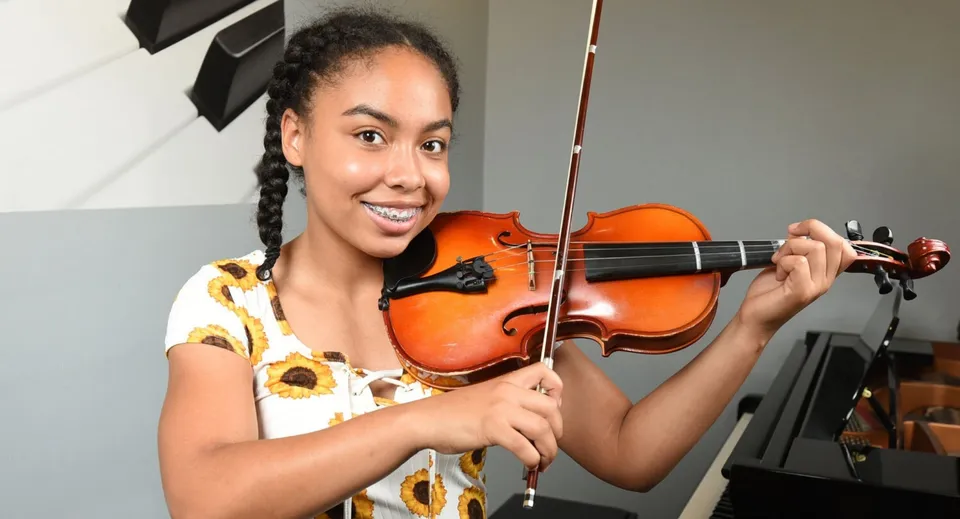 Una studentessa della London Central Secondary School suona il violino in una stanza con strumenti musicali sullo sfondo.