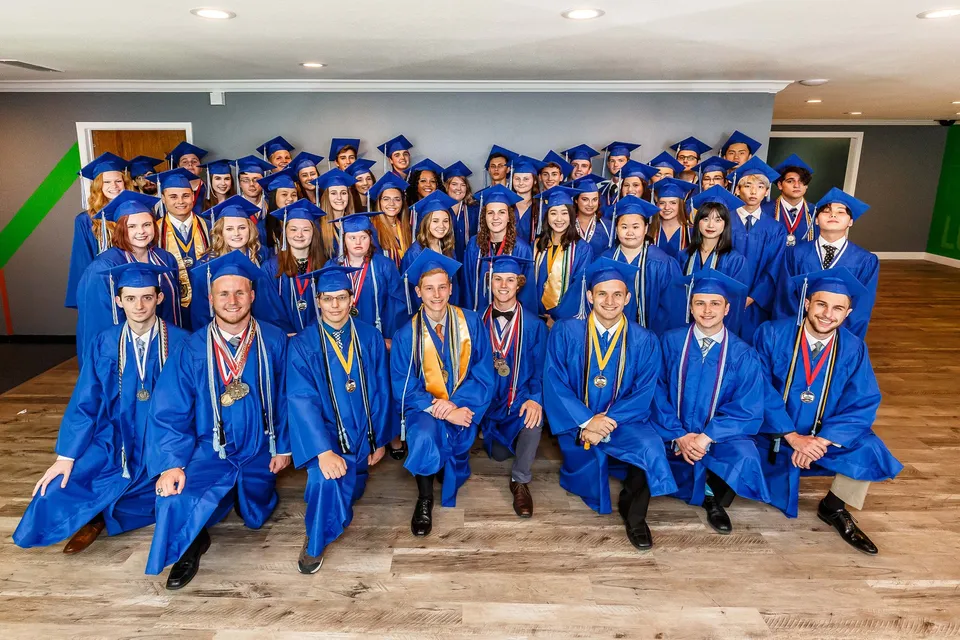 Un grande gruppo di diplomati in toga blu si trova nell'aula della Rocky Bayou Christian High School.