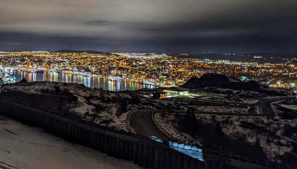 Vista notturna di una città illuminata e del porto da una collina innevata nella regione della St. Kevin's High School.
