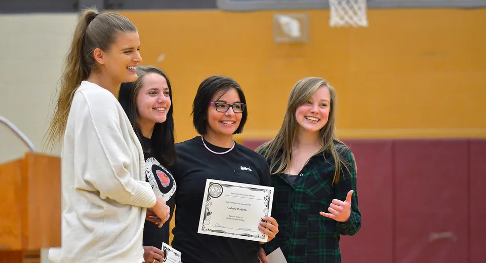 Quattro studentesse della Sparwood Secondary School sorridono in una palestra, una di loro tiene in mano un attestato.