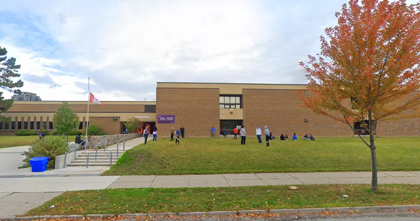 L'edificio in mattoni del Martingrove Collegiate Institute si trova davanti a un'area verde con alberi e un marciapiede con persone.