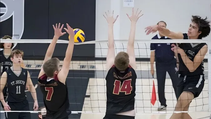 Estudiantes de la St. Joseph High School juegan al voleibol y tratan de bloquear el balón en la red.