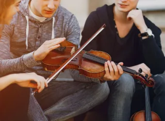 Tres jóvenes de la Ottawa Sports Academy Private School están sentados juntos observando un violín.