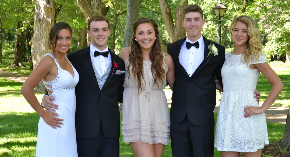 Un gruppo di cinque persone in abiti formali si trova nel giardino del Birchmount Park Collegiate Institute.